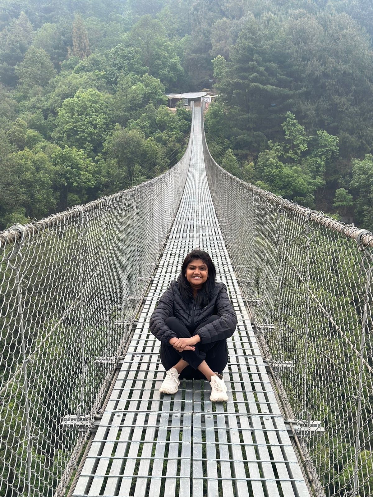 Meenal, founder of TakeMeAway Journeys, sitting on a suspension bridge surrounded by forest